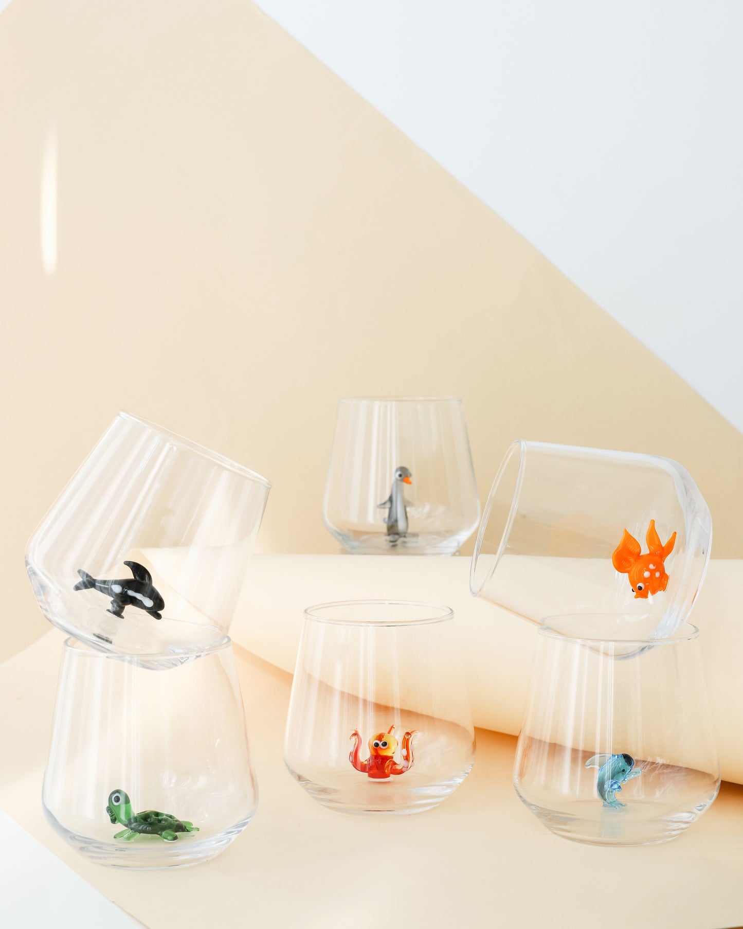 A set of clear drinking glasses with various handmade animal figures inside, displayed against a neutral background.