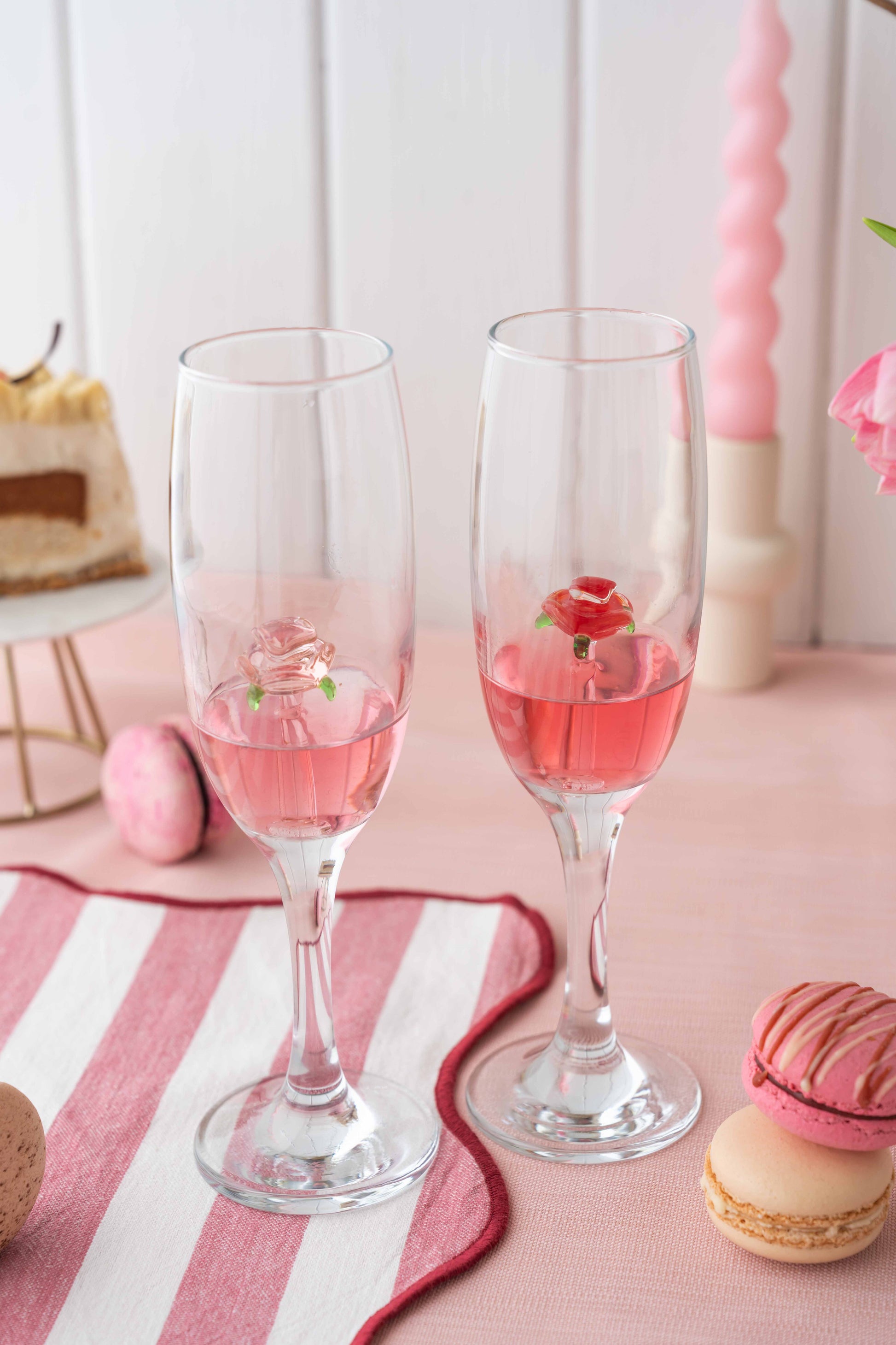 Two glasses of pink cocktail with a flower on a pink and white striped tablecloth.